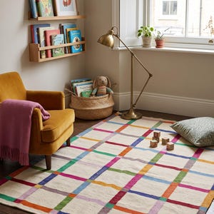 Peut inclure: Un tapis rectangulaire avec une base de couleur crème orné d'un motif à carreaux composé de lignes entrecroisées dans des tons vifs de bleu, vert, rouge, orange et violet. Le tapis est posé sur un parquet sombre dans une pièce avec un fauteuil jaune.