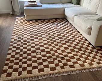 May include: A brown and white checkered rug with a fringe border. The rug is in front of a white sectional sofa.