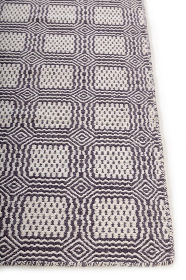 May include: A rectangular area rug featuring a repeating geometric pattern of dark gray and off-white squares. The design consists of interconnected diamond shapes and rounded squares with a textured, woven appearance across the entire surface.
