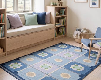 May include: A rectangular area rug featuring a grid pattern of alternating light blue, dark blue, and lavender squares. Each square contains a centered geometric motif in shades of cream, pale green, and white, creating a repeating tiled design.