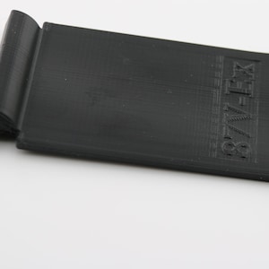 May include: Black plastic phone stand with a cutout for a phone and the text "87V-FX" printed on the side.