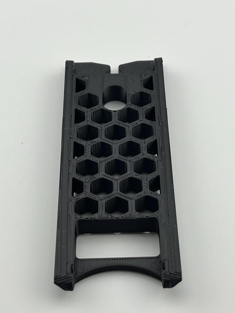 May include: A black, rectangular object with a honeycomb pattern. The object has a series of hexagonal openings and a curved bottom. The top has a notch and a circular opening. The object is made of a matte black material.