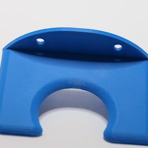 May include: A blue plastic wall mount with a curved top and a circular cutout. The mount has three holes for screws.