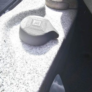 Op de afbeelding: Een close-up van een grijze jacuzzi met twee grijze hoofdsteunen. De hoofdsteunen zijn glad en afgerond, met een gestructureerd, vierkant ontwerp op de bovenkant van één. De jacuzzi heeft een gespikkelde, granietachtige oppervlakte.