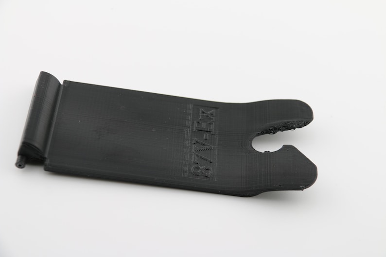 May include: Black plastic phone stand with a cutout for a phone and the text "87V-FX" printed on the side.