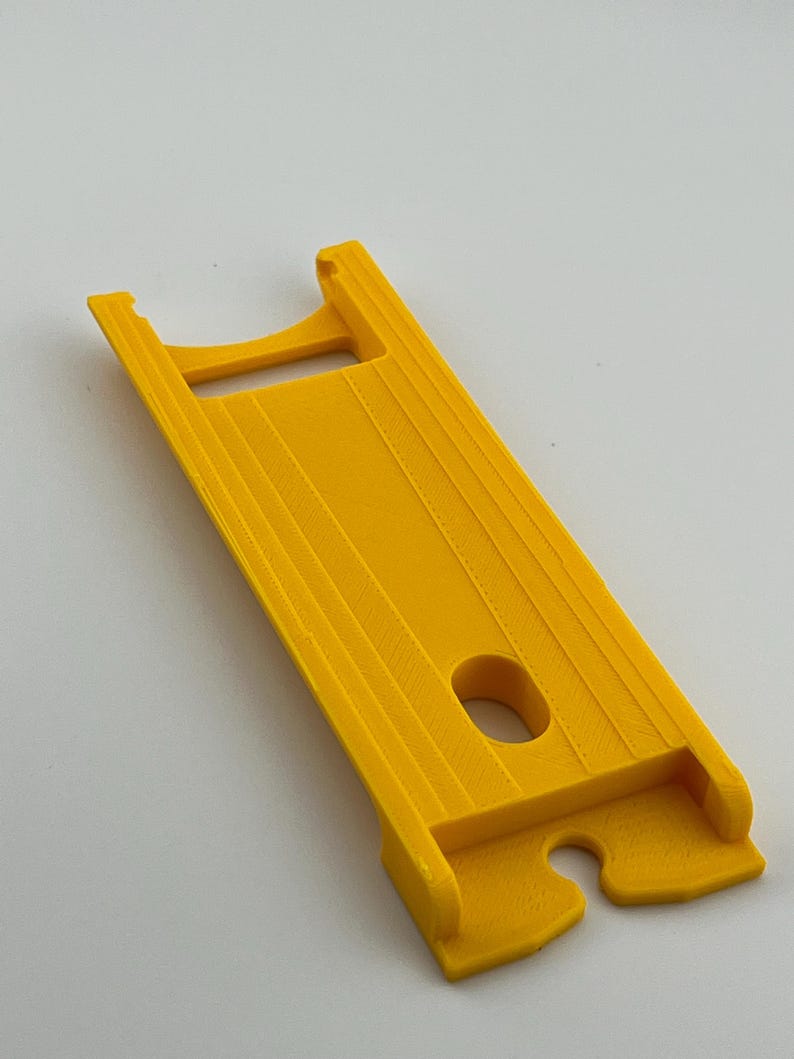 Puede incluir: Una herramienta de pl&aacute;stico amarillo brillante con un cuerpo rectangular y una abertura similar a un asa. Tiene una serie de crestas paralelas a lo largo de su longitud y un agujero circular cerca del centro. El otro extremo tiene un recorte curvo.