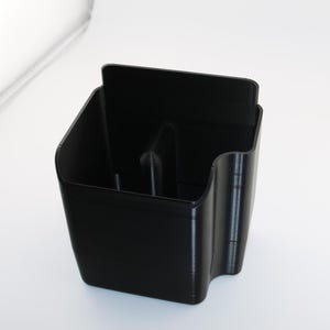 May include: A black plastic organizer with three compartments. The organizer is designed to hold small items, such as pens, pencils, or other office supplies.