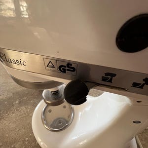 Könnte beinhalten: Ein weißer Küchenmixer mit einem silbernen Bedienfeld und einem schwarzen Knopf. Der Mixer hat eine silberne Schüssel und einen silbernen Hebel. Der Text "Classic" ist auf dem Bedienfeld sichtbar. Der Text "GS" ist auf einem Aufkleber auf dem Bedienfeld sichtbar.