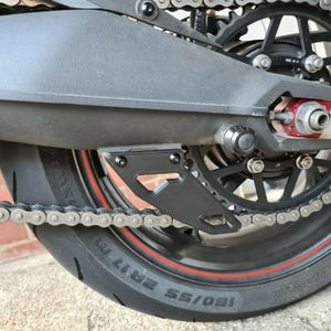 Puede incluir: Guardabarros de cadena de motocicleta negro con una cadena negra y una franja roja en el neum&aacute;tico. El neum&aacute;tico est&aacute; etiquetado "180/55 ZR17"