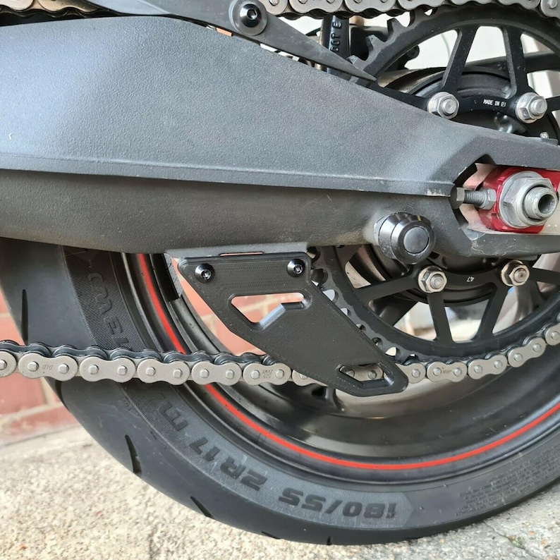 Puede incluir: Guardabarros de cadena de motocicleta negro con una cadena negra y una franja roja en el neum&aacute;tico. El neum&aacute;tico est&aacute; etiquetado "180/55 ZR17"