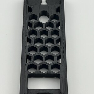 May include: A black, rectangular 3D-printed object with a honeycomb pattern. The object has a curved bottom and a notched top with a circular hole. The design features a series of hexagonal cells, creating an open, geometric structure.