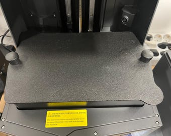 May include: Close-up of a black 3D printer with a warning label that reads: "The resin level cannot exceed the MAX line in the tank, otherwise it may leak and damage the machine."