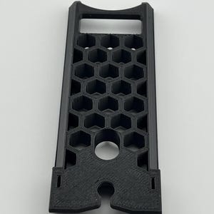 May include: A black, rectangular 3D-printed object with a honeycomb pattern. It features a handle at the top and a circular hole near the bottom. The object is designed with a series of hexagonal cells.