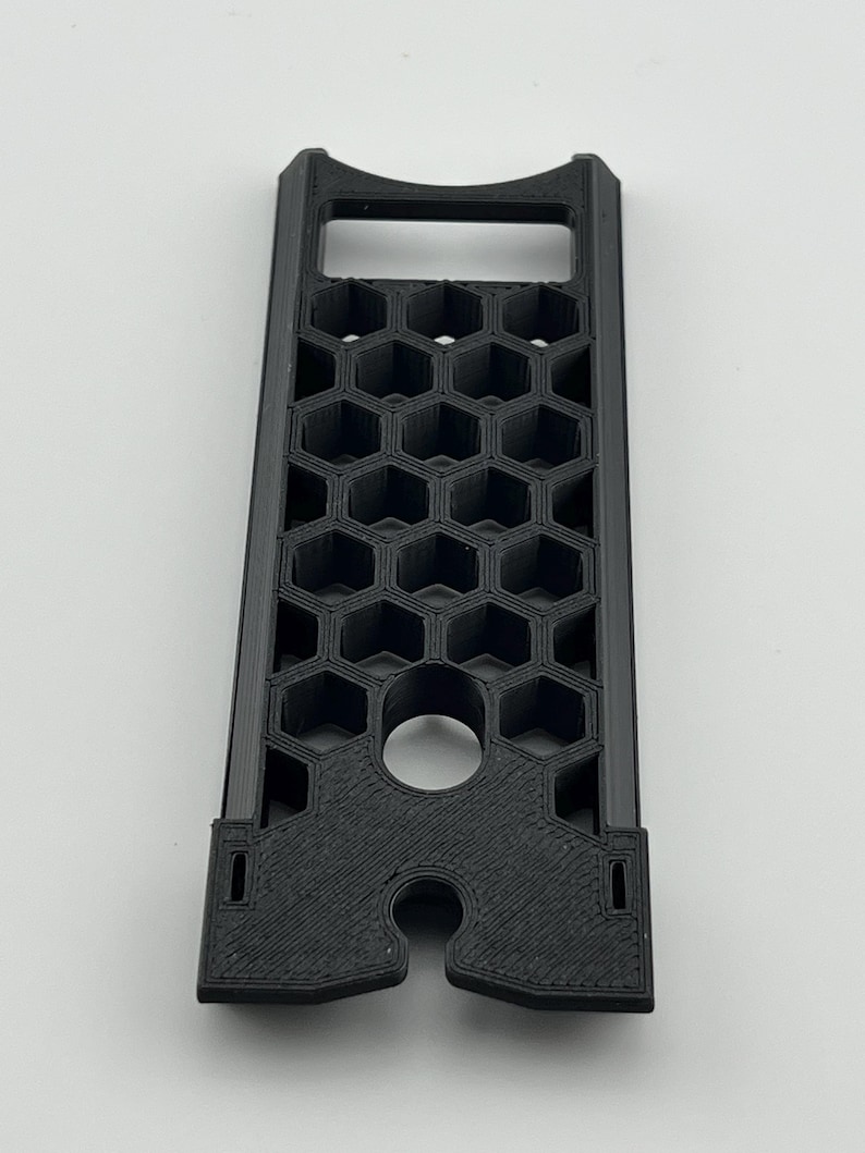 May include: A black, rectangular 3D-printed object with a honeycomb pattern. It features a handle at the top and a circular hole near the bottom. The object is designed with a series of hexagonal cells.