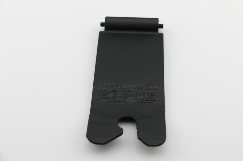 May include: Black plastic strap with a cut-out for a buckle and the text "87W-1EX" printed on it.
