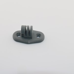 May include: Grey plastic mount with a GoPro camera mount attachment. The mount has two holes on the bottom for attaching to a surface.