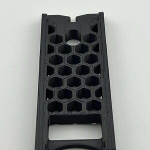 May include: A black, rectangular object with a honeycomb pattern. The object has a series of hexagonal openings and a circular hole near the top. The bottom has a curved opening. The object is made of a matte black material.