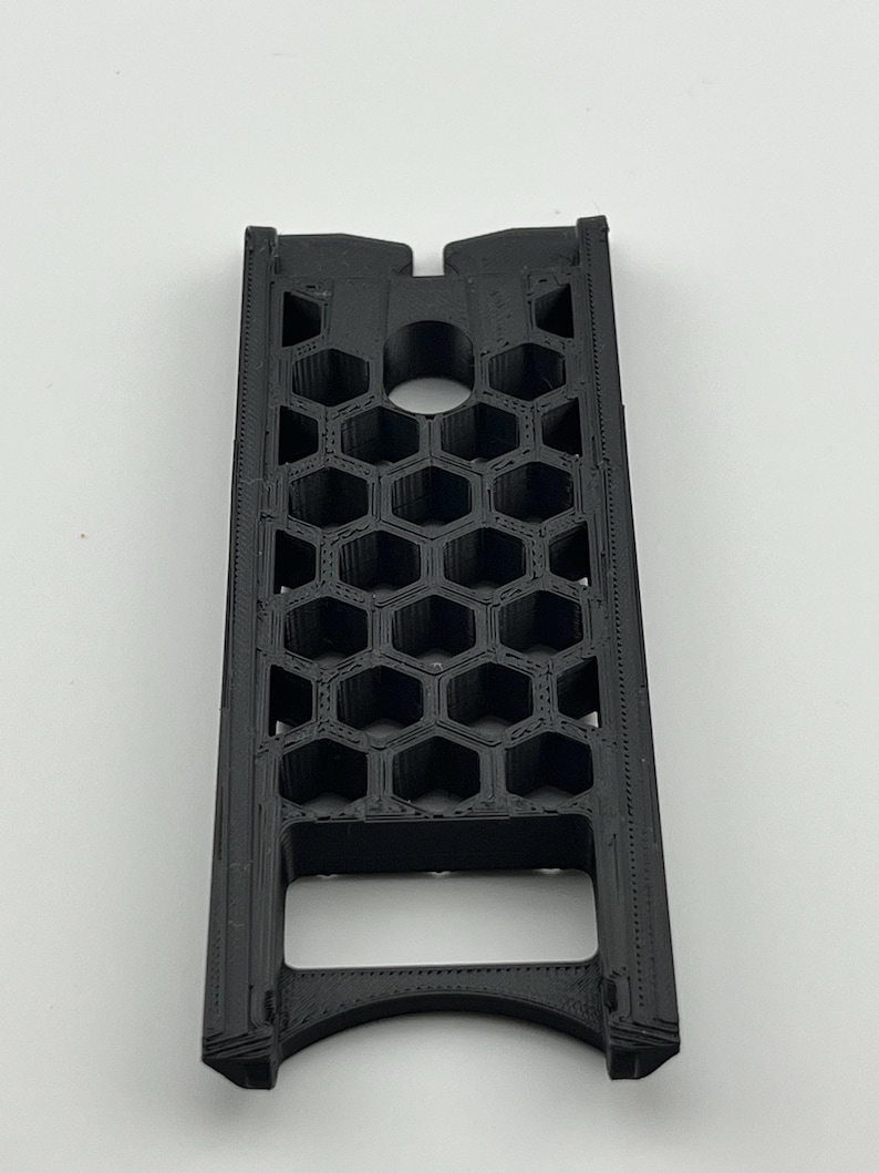 May include: A black, rectangular object with a honeycomb pattern. The object has a series of hexagonal openings and a circular hole near the top. The bottom has a curved opening. The object is made of a matte black material.