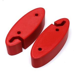 Puede incluir: Dos objetos rojos de forma ovalada, con superficie texturizada y un agujero perforado en cada uno. Un objeto tiene una muesca curva en un extremo. Los objetos son probablemente componentes o piezas de un artículo más grande.