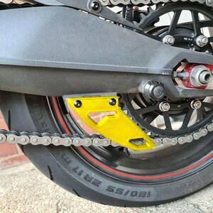 Puede incluir: Un protector de cadena de motocicleta amarillo con una cadena negra y un neum&aacute;tico negro con una franja roja. El neum&aacute;tico tiene el texto "180/55 ZR17" impreso.