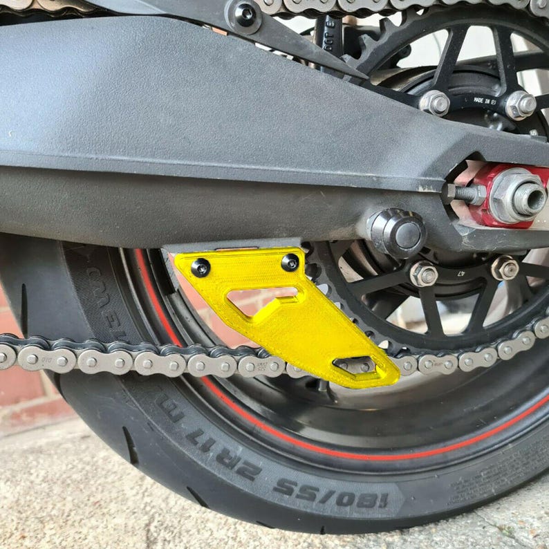 Puede incluir: Un protector de cadena de motocicleta amarillo con una cadena negra y un neum&aacute;tico negro con una franja roja. El neum&aacute;tico tiene el texto "180/55 ZR17" impreso.