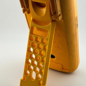 May include: A yellow digital multimeter with a built-in stand. The stand has a honeycomb design. The multimeter has a label with the number "11440054".