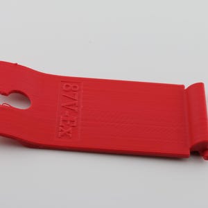 May include: A red plastic tool with a hook on one end and the text "87V-EX" printed on the other end.