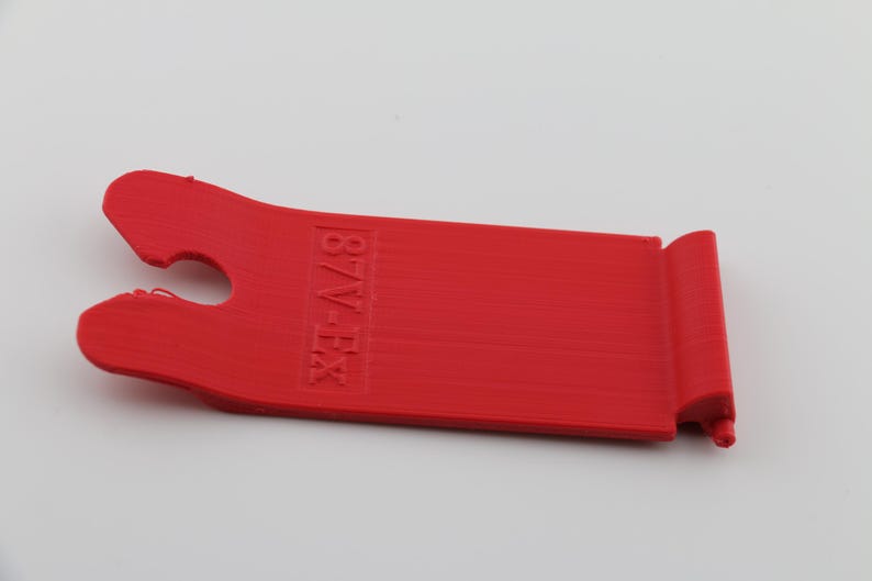 May include: A red plastic tool with a hook on one end and the text "87V-EX" printed on the other end.
