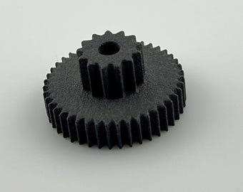 Könnte beinhalten: Ein schwarzes, 3D-gedrucktes Zahnrad mit einem zentralen Loch und zwei Zahnreihen. Das Zahnrad ist vor einem schlichten weißen Hintergrund platziert, der sein mechanisches Design und seine Textur hervorhebt. Der Durchmesser des Zahnrads beträgt ca. 5 cm.