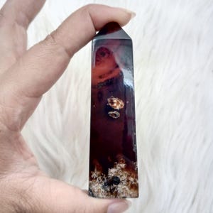 May include: A dark red and black agate crystal point with white inclusions. The crystal is polished and has a smooth, glossy finish.