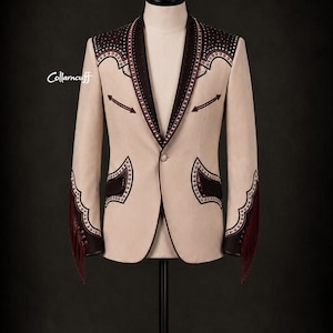 May include: A beige blazer with dark brown accents and decorative stitching. The blazer features fringe on the sleeves and is displayed on a mannequin. The collar and pockets are trimmed with dark brown fabric.