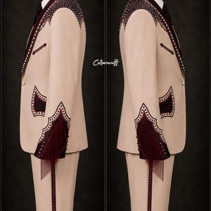 May include: A beige suit with intricate burgundy embroidery and fringe detailing. The suit features a notched lapel, decorative shoulder accents, and fringe on the sleeves. The text "Collarncuff" is visible on the side. The suit is displayed on a mannequin.