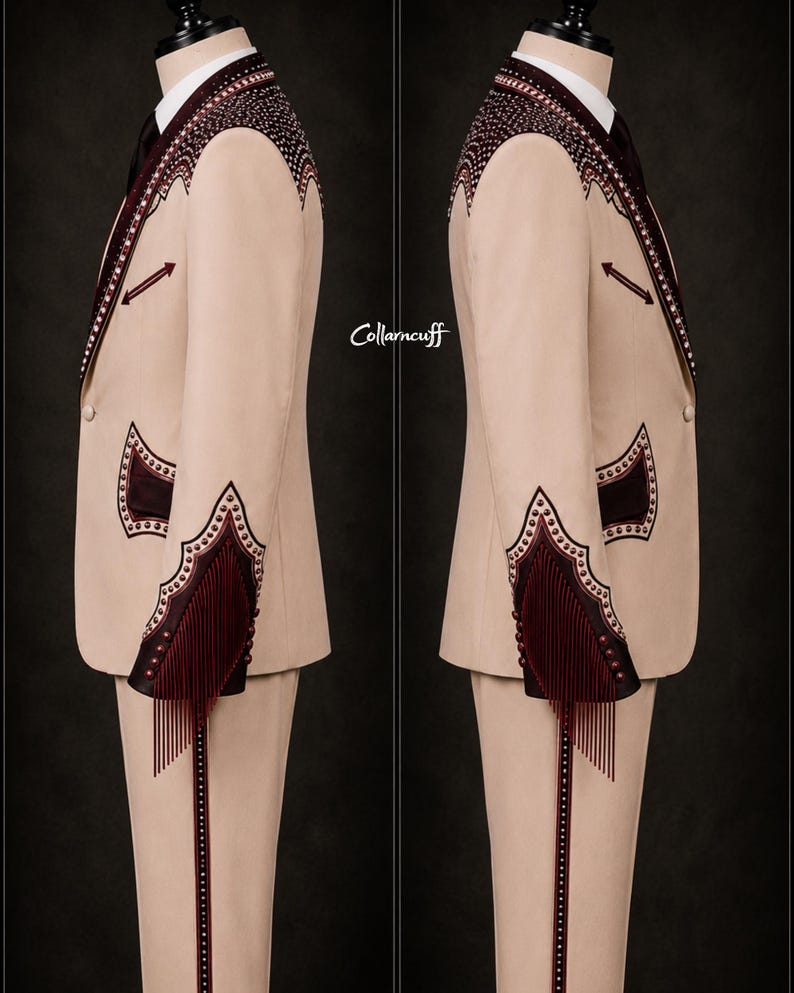 May include: A beige suit with intricate burgundy embroidery and fringe detailing. The suit features a notched lapel, decorative shoulder accents, and fringe on the sleeves. The text "Collarncuff" is visible on the side. The suit is displayed on a mannequin.