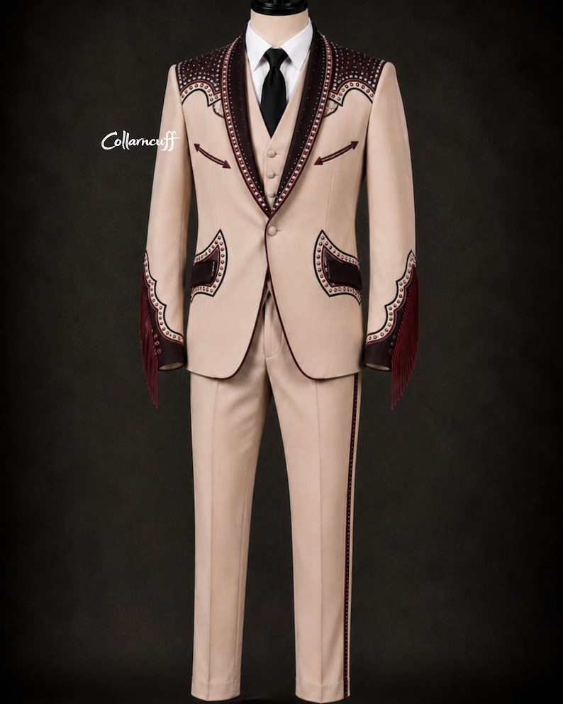 May include: A tan suit with decorative dark brown accents, including fringe on the sleeves. The suit features a blazer, vest, and trousers, with a black tie and white shirt. The suit has decorative stitching and trim.