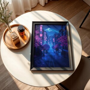 May include: A framed print of a digital painting depicting a nighttime cityscape with a mountain in the background. The city is illuminated with neon lights and pink cherry blossoms. The print is in a black frame.