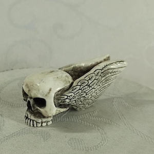 May include: A white ceramic skull with wings. The skull has detailed features and the wings are intricately carved.