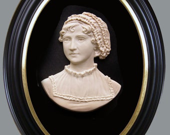 May include: A white ceramic bust of a woman wearing a white lace cap, framed in a black oval frame with a gold trim.