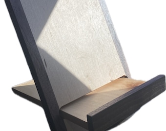 Puede incluir: Un soporte de libros de madera con una base de madera clara y un marco de madera oscura. El soporte está inclinado para sostener un libro o una tableta.