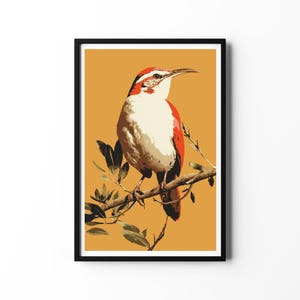Puede incluir: Una impresión artística enmarcada que presenta una ilustración estilizada de un pájaro posado en una rama. El pájaro tiene plumaje rojo, blanco y marrón, con un pico largo. El fondo es de color amarillo mostaza y la impresión está enmarcada en negro.
