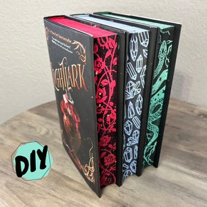 May include: Four hardback books with decorative edges. The first book has a black cover with the title "NIGHTARK" in red and gold lettering. The edges are red. The other books have decorative edges with red roses, blue crystals, and green snakes.