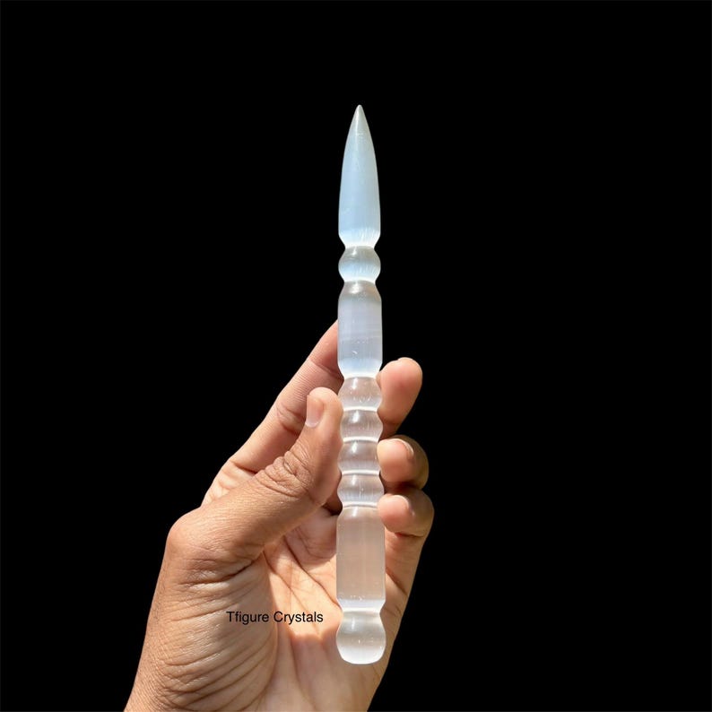 K&ouml;nnte beinhalten: Ein klarer, l&auml;nglicher Kristallstab mit einer Spitze und einem strukturierten Griff. Der Stab wird vor einem schwarzen Hintergrund gehalten. Der Kristallstab ist etwa 18 cm lang.