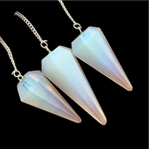 Puede incluir: Tres péndulos de cristal facetado con colores iridiscentes, suspendidos por cadenas plateadas. Los cristales tienen forma de cono, con una punta y una parte superior plana y geométrica. El fondo es negro.