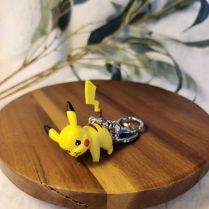 May include: A yellow Pikachu keyring with a silver key ring. The keyring is made of plastic and has a cartoonish design.