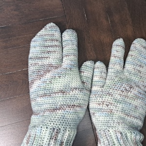 Op de afbeelding: Een paar gebreide wanten met een gesplitst vingerontwerp. De wanten zijn gemaakt van lichtblauw, bruin en wit garen.