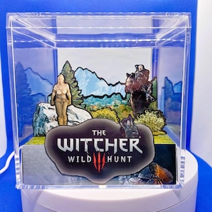 May include: A clear acrylic display box depicting a scene from "The Witcher 3: Wild Hunt." The scene includes character cutouts, a mountain backdrop, and the game's logo. The box is illuminated from below, creating a diorama effect.