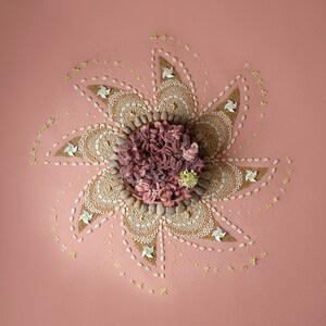 May include: A pink and white mandala made of small stones and white flowers on a pink background.