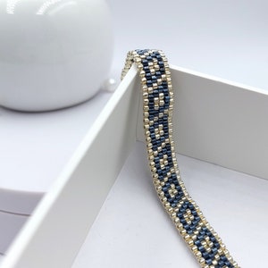 May include: A beaded bracelet with a geometric pattern in shades of blue and gold.