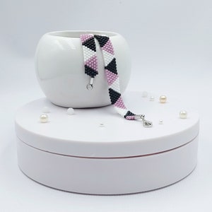 Könnte beinhalten: Zwei Armbänder aus schwarzen, weißen und rosafarbenen Perlen mit silbernen Verschlüssen auf einer weißen Oberfläche.