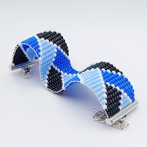 May include: A blue, black, and white beaded bracelet with silver clasps. The bracelet is made of small, round beads that are woven together in a geometric pattern.