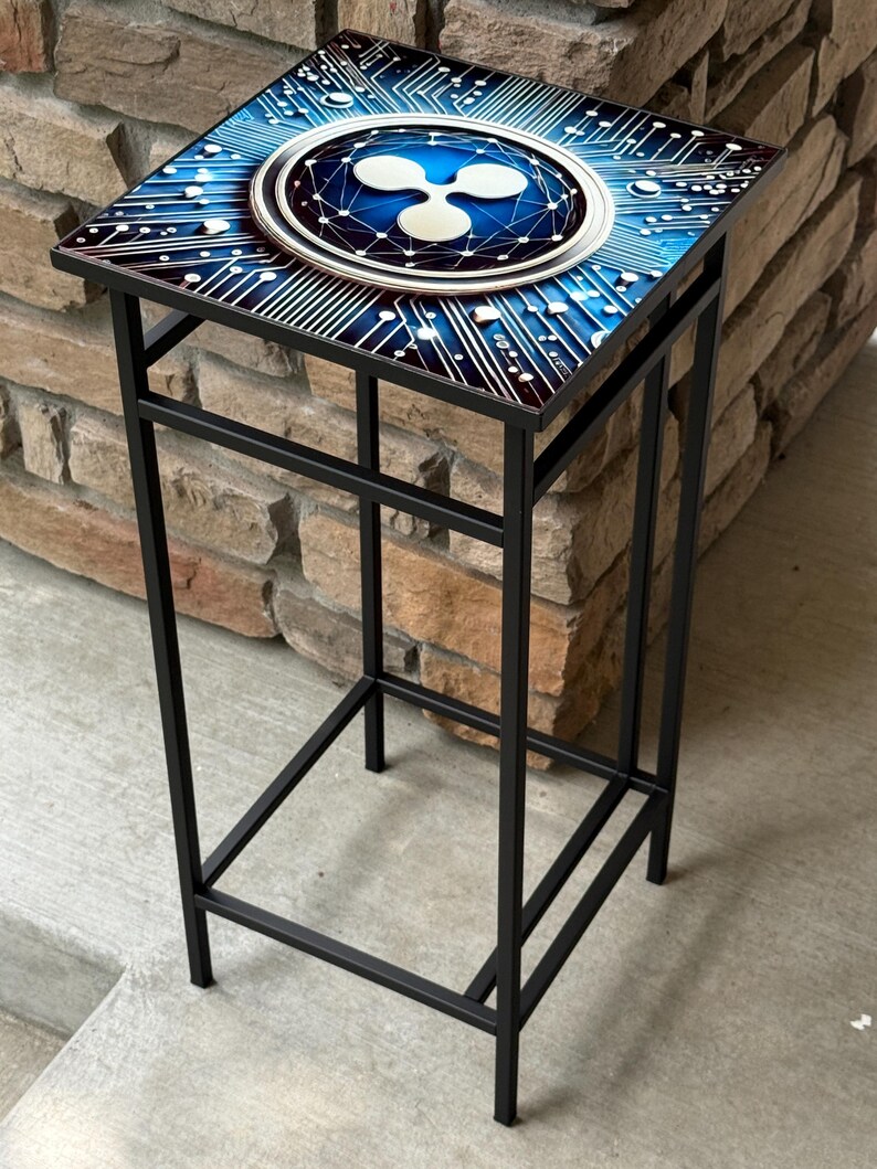 K&ouml;nnte beinhalten: Ein schwarzer Metall-Beistelltisch mit quadratischer Platte mit blauem und wei&szlig;em Design. Das Design umfasst ein Leiterplattenmuster und ein zentrales Ripple-Logo. Der Tisch ist etwa 61 cm hoch.